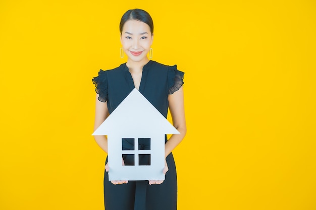 Portrait belle jeune femme asiatique avec maison ou papier à la maison signe sur jaune