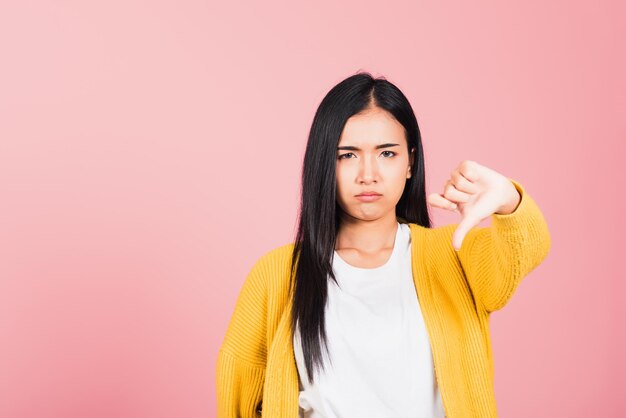 Portrait d'une belle jeune femme asiatique malheureuse geste négatif montrant les pouces vers le bas