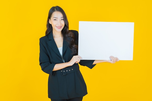 Portrait belle jeune femme asiatique avec panneau blanc vide sur jaune