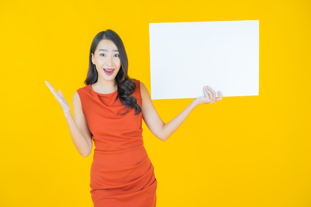 Portrait belle jeune femme asiatique avec panneau blanc vide sur jaune