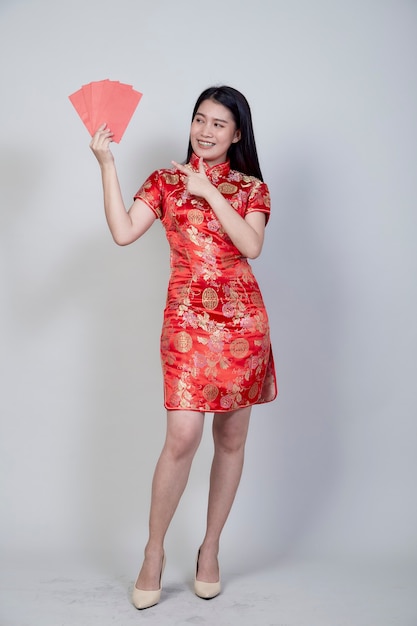 Portrait belle jeune femme asiatique porter une robe chinoise tenant un paquet rouge cadeau monétaire de félicitations salutation bonne année 2021 isolé sur fond gris clair avec espace copie