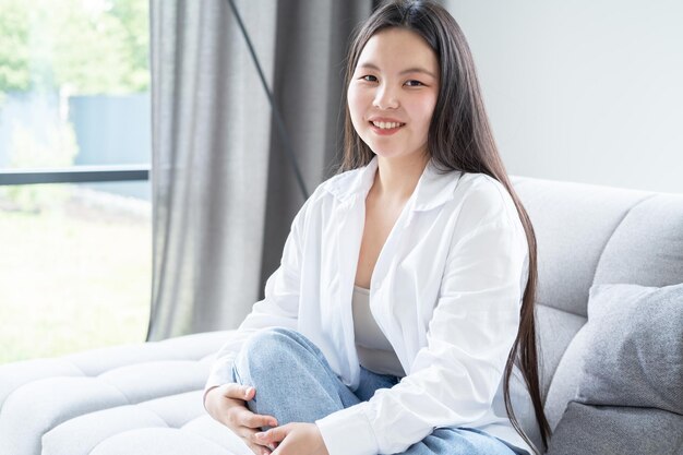 portrait d'une belle jeune femme asiatique souriante aux longs cheveux noirs en chemise blanche à la maison moderne