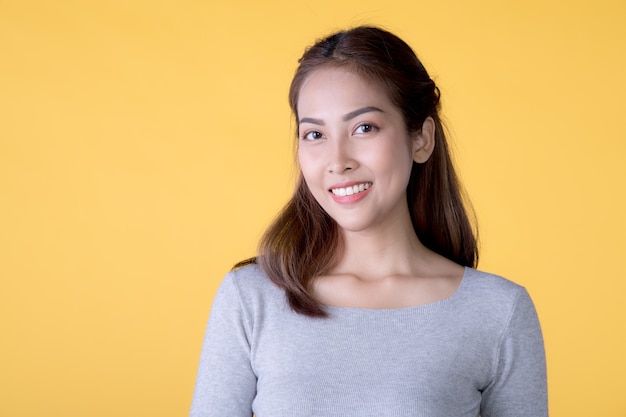 Portrait d'une belle jeune femme asiatique souriante dans des vêtements décontractés, isolé sur fond jaune, regardant la caméra