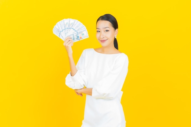 Portrait belle jeune femme asiatique sourire avec beaucoup d'argent et d'argent sur jaune
