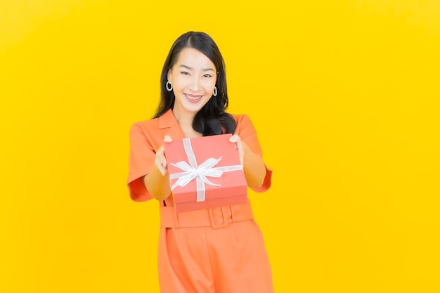 Portrait belle jeune femme asiatique sourire avec boîte-cadeau rouge sur jaune