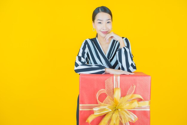 Portrait belle jeune femme asiatique sourire avec boîte-cadeau rouge sur jaune