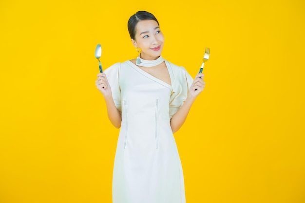 Portrait belle jeune femme asiatique sourire avec cuillère et fourchette sur fond de couleur