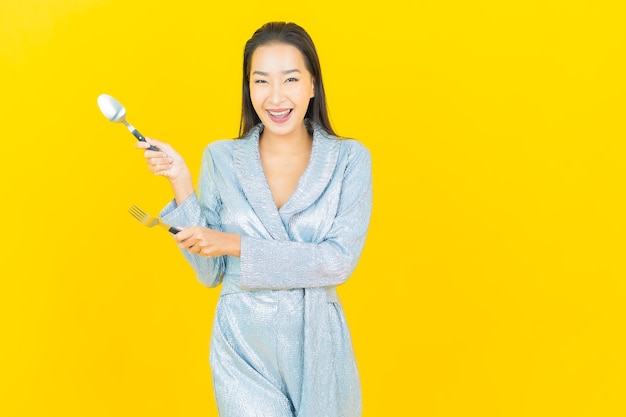 Portrait belle jeune femme asiatique sourire avec cuillère et fourchette sur mur jaune