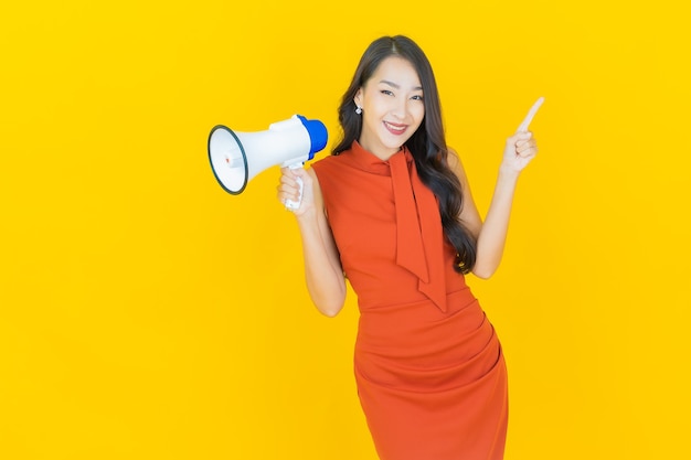 Portrait belle jeune femme asiatique sourire avec mégaphone sur jaune