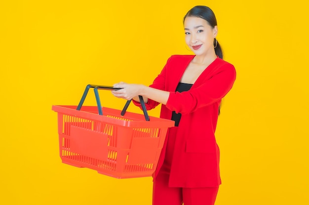 Portrait belle jeune femme asiatique sourire avec panier d'épicerie du supermarché sur jaune