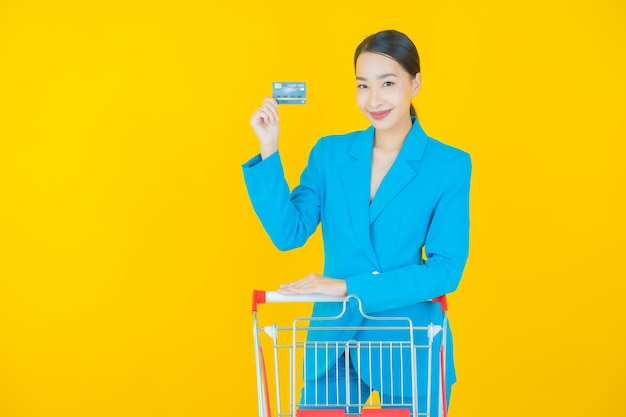 Portrait belle jeune femme asiatique sourire avec panier d'épicerie du supermarché sur jaune