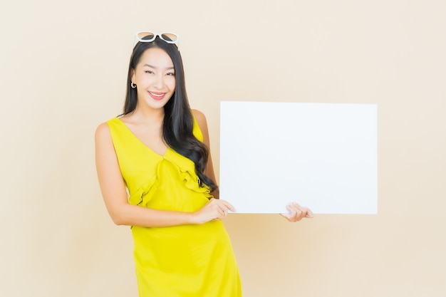 Portrait belle jeune femme asiatique sourire avec tableau blanc vide sur mur jaune