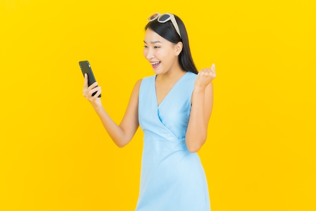 Portrait belle jeune femme asiatique sourire avec téléphone mobile intelligent sur le mur de couleur jaune