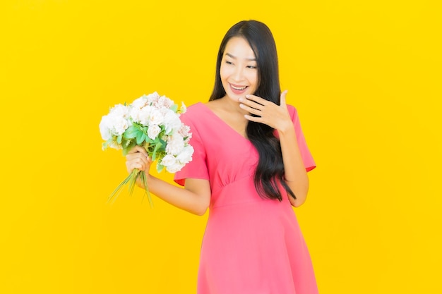 Portrait belle jeune femme asiatique sourit avec bouquet de fleurs sur mur jaune