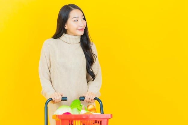 Portrait Belle Jeune Femme Asiatique Sourit Avec Panier D'épicerie Du Supermarché Sur Mur Jaune