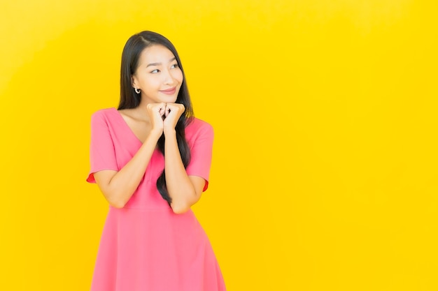 Portrait de la belle jeune femme asiatique sourit en robe rose sur mur jaune