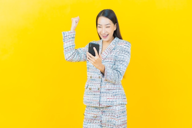 Portrait belle jeune femme asiatique sourit avec un téléphone mobile intelligent sur un mur de couleur