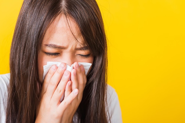 Portrait d'une belle jeune femme asiatique triste qu'elle pleure essuyer le mucus avec du tissu, gros plan d'une jolie fille éternuant sinus à l'aide d'une serviette pour essuyer la morve du nez, prise de vue en studio isolée sur fond jaune