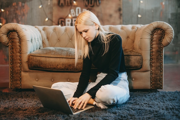 Portrait d'une belle jeune femme assise sur le sol et travaillant sur un ordinateur portable à la maison.