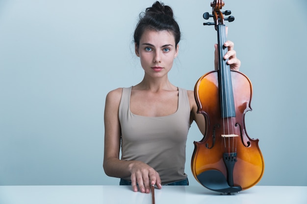 Portrait d'une belle jeune femme assise à la table avec un violon isolé sur fond bleu