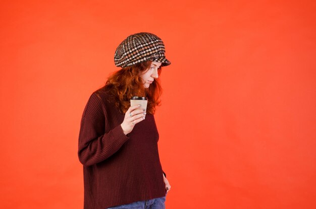 portrait de la belle jeune femme aux cheveux bouclés rouges, yeux bleus. fond rouge. Buvant du café