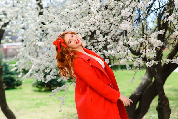 Portrait de la belle jeune femme aux cheveux roux en robe blanche en fleurs de printemps, fleur