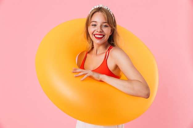 Portrait d'une belle jeune femme aux longs cheveux bouclés souriante et tenant un anneau en caoutchouc de natation isolé sur un mur rose