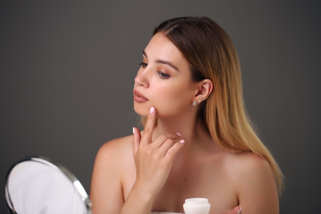 Portrait d'une belle jeune femme blonde à l'aide de produits cosmétiques de soins de la peau