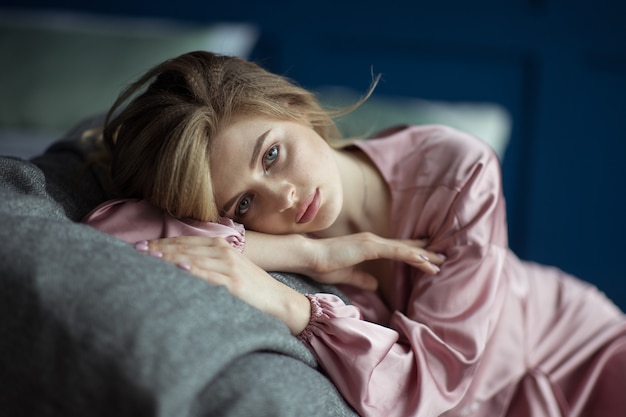 Portrait d'une belle jeune femme blonde aux cheveux ondulés dans un peignoir rose avec une coupe profonde.