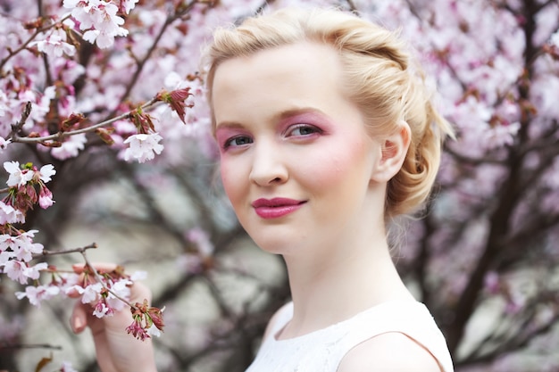 Portrait d'une belle jeune femme blonde sur un cerisier en fleurs au printemps