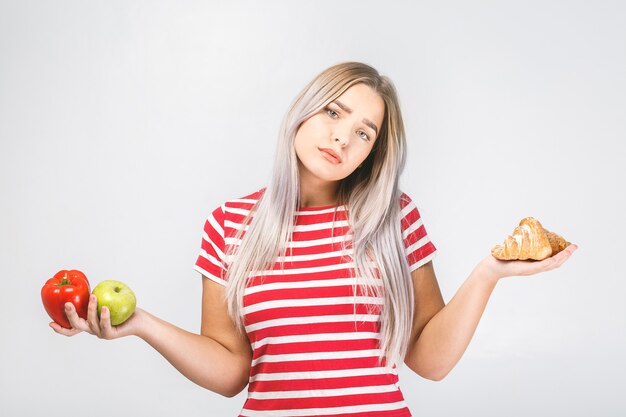 Portrait d'une belle jeune femme blonde confuse en choisissant entre une alimentation saine et malsaine