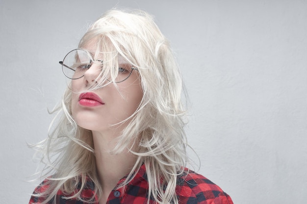 Portrait d'une belle jeune femme blonde à lunettes rondes et aux lèvres charnues dans une chemise à carreaux rouge sur fond blanc