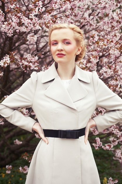 Portrait d'une belle jeune femme blonde par des cerisiers en fleurs au printemps