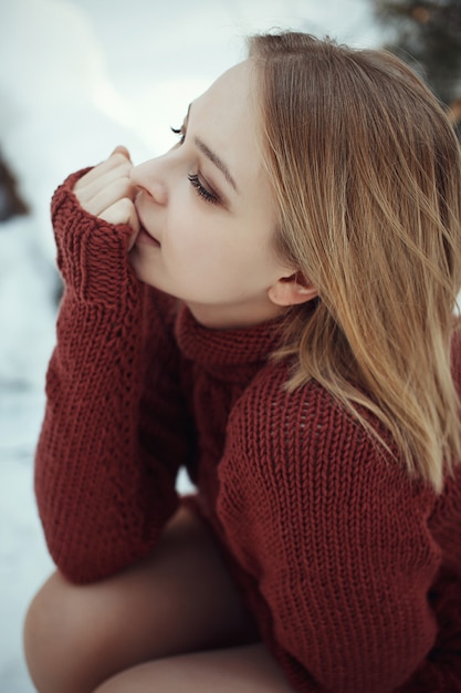 Portrait d'une belle jeune femme blonde en pull posant dans le parc d'hiver. Journée ensoleillée dans la forêt.