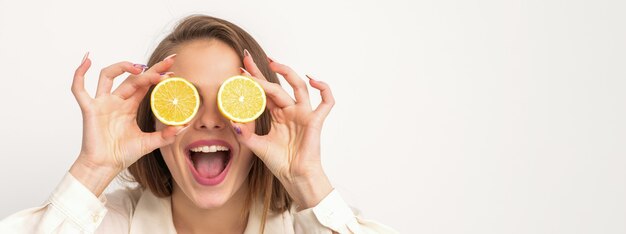 Portrait d'une belle jeune femme avec une bouche ouverte tenant deux tranches d'orange à ses yeux sur un fond blanc