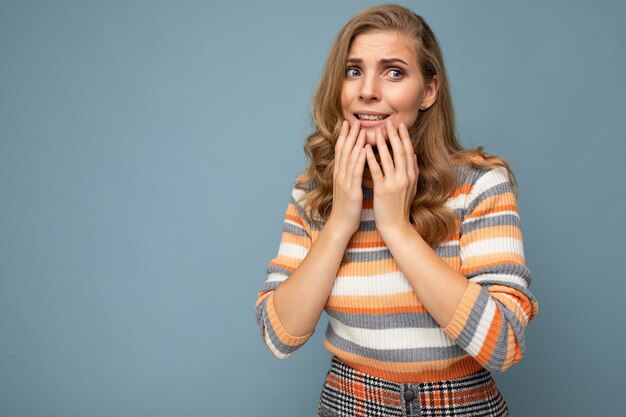 Portrait de la belle jeune femme bouclée blonde avec des émotions sincères portant élégant pull rayé