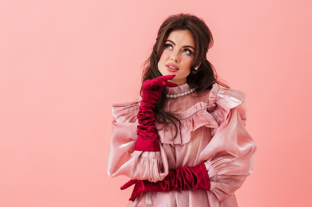 Portrait d'une belle jeune femme brune avec un maquillage lumineux portant des vêtements à la mode debout isolé sur un mur rose, posant