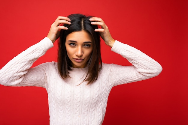 Portrait d'une belle jeune femme brune portant un maillot tricoté isolé sur fond rouge avec un espace libre et touchant les cheveux courts