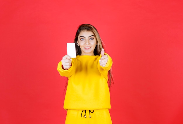 Portrait d'une belle jeune femme avec une carte de visite vierge donnant les pouces vers le haut