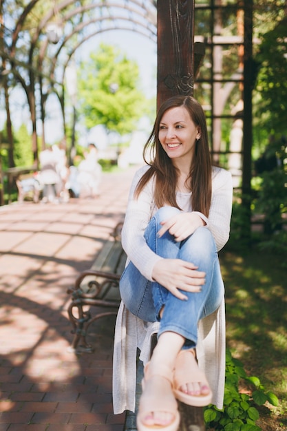 Portrait d'une belle jeune femme caucasienne avec un charmant sourire portant des vêtements légers et décontractés. Femme souriante assise sous une arche dans le parc de la ville dans la rue à l'extérieur sur la nature printanière. Concept de mode de vie