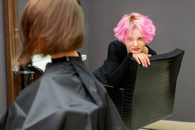 Portrait d'une belle jeune femme caucasienne avec une nouvelle coiffure rose courte assise sur une chaise dans un salon de coiffure