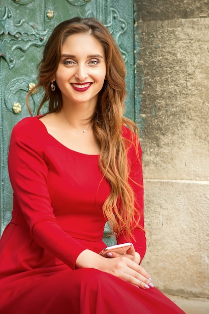 Portrait d'une belle jeune femme caucasienne voyageant assis à la porte avec smartphone souriant