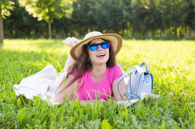 Portrait de belle jeune femme avec chapeau et lunettes de soleil se trouvant dans le parc en pique-nique