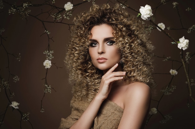 Portrait de belle jeune femme avec une coiffure afro et beau maquillage avec beaucoup de fleurs blanches sur le mur