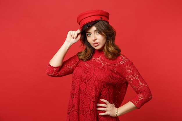 Portrait d'une belle jeune femme confiante en robe de dentelle tenant une casquette regardant la caméra isolée sur fond de mur rouge vif en studio. Émotions sincères des gens, concept de style de vie. Maquette de l'espace de copie.