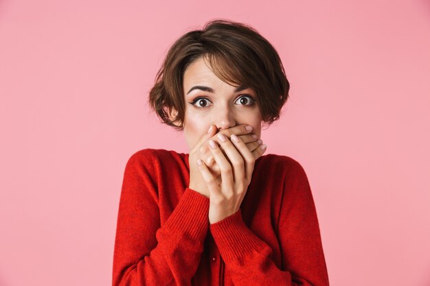 Portrait d'une belle jeune femme confus choqué portant des vêtements rouges debout isolé sur fond rose