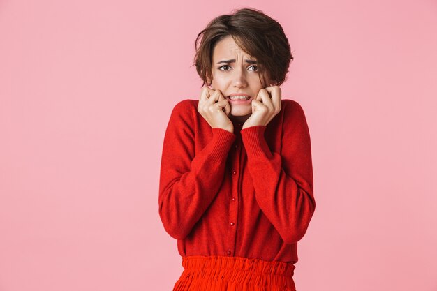 Portrait d'une belle jeune femme confus choqué portant des vêtements rouges debout isolé sur fond rose