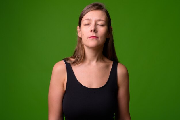 Portrait de la belle jeune femme contre le mur vert