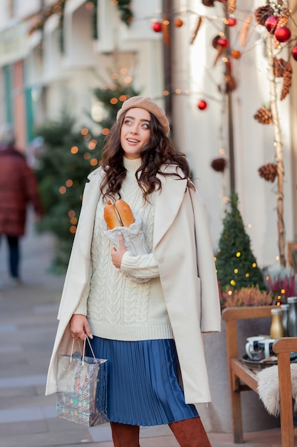 Portrait d'une belle jeune femme dans un béret dans une ville européenne. Jeune femme tient un sac en papier avec des baguettes. Noël. Vacances.