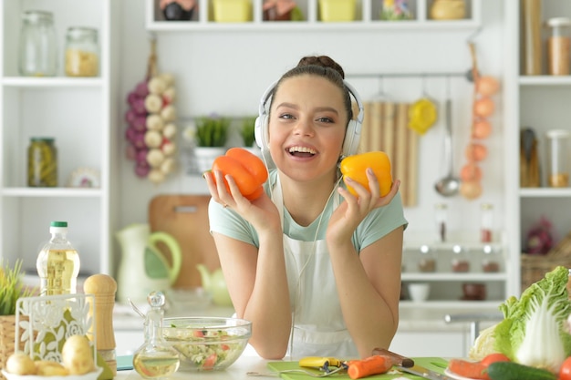 Portrait d'une belle jeune femme dans des écouteurs préparant de la salade à la maison